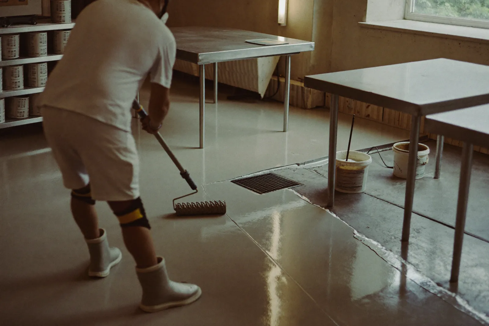 Installer rolling light gray epoxy across a restaurant kitchen floor near a floor drain