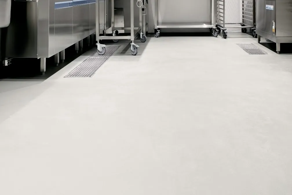Seamless light gray coated floor in a commercial kitchen with stainless carts and trench drains