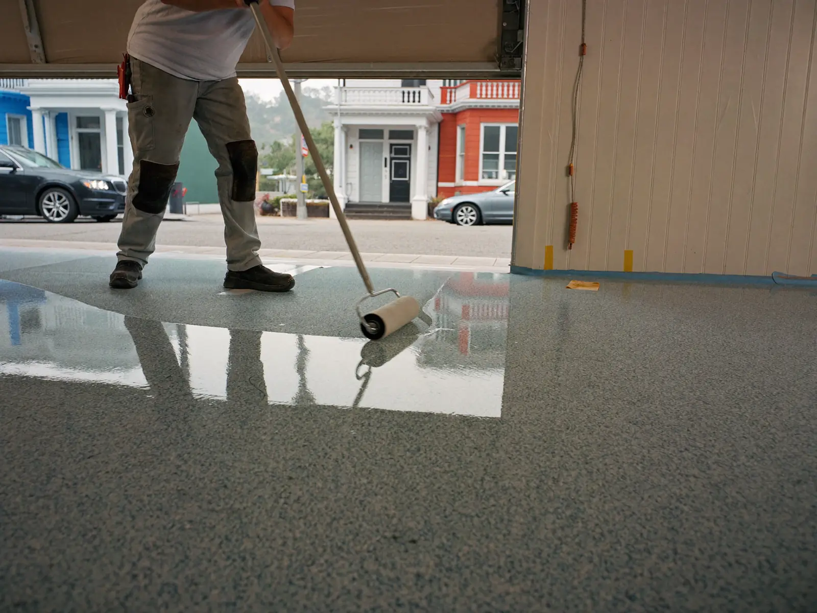 Installer rolling a clear polyaspartic topcoat over a blue-gray flake garage floor